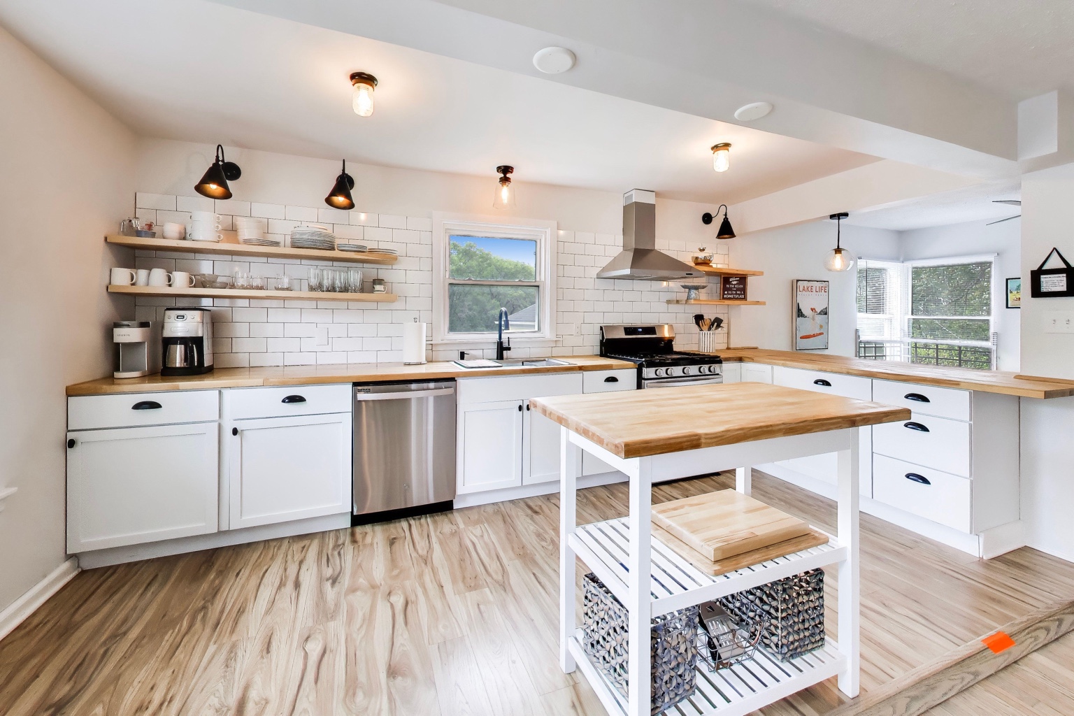 Bright cottage kitchen with white cabinetry, butcher-block counters, stainless appliances, and a central island